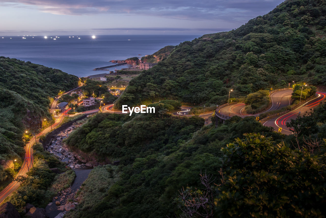 High angle view of illuminated city by sea against sky