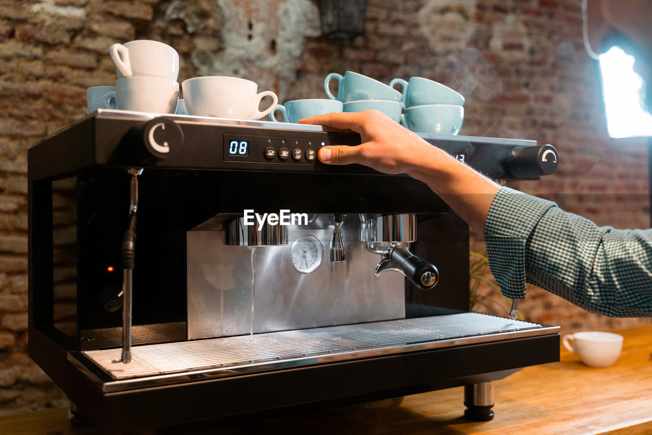 Unrecognizable crop bartender with portafilter preparing beverage in modern coffeemaker while working in cafe