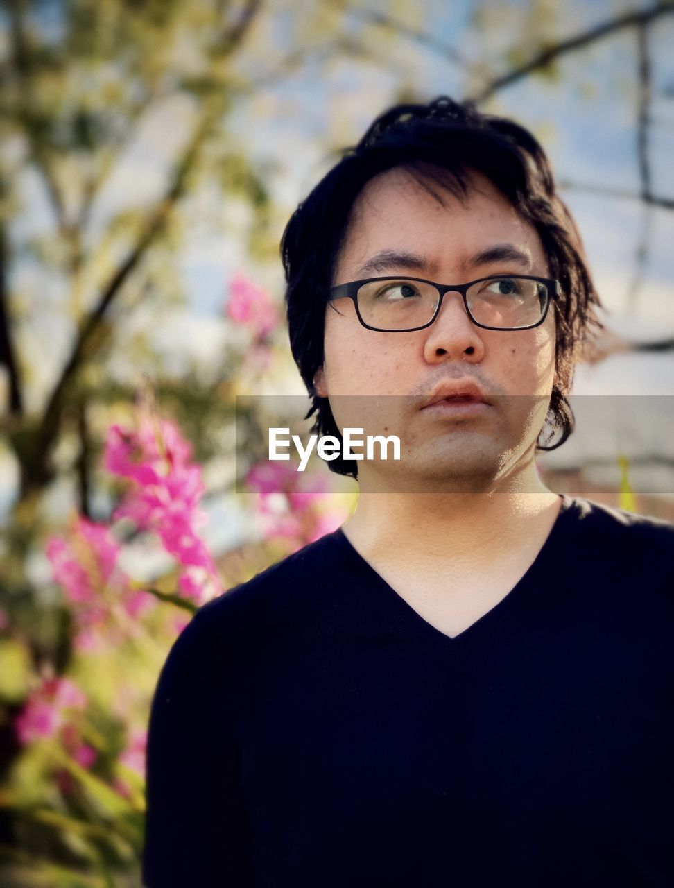 Portrait of young man wearing eyeglasses against pink flowering plants.