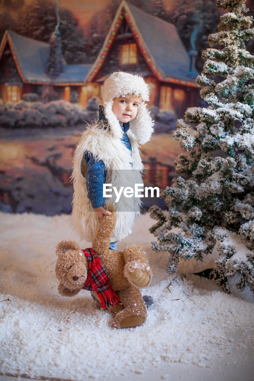 Cute girl holding stuffed toy standing by christmas tree