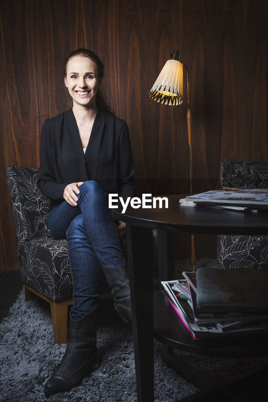 Full length portrait of happy businesswoman sitting on chair in office lobby