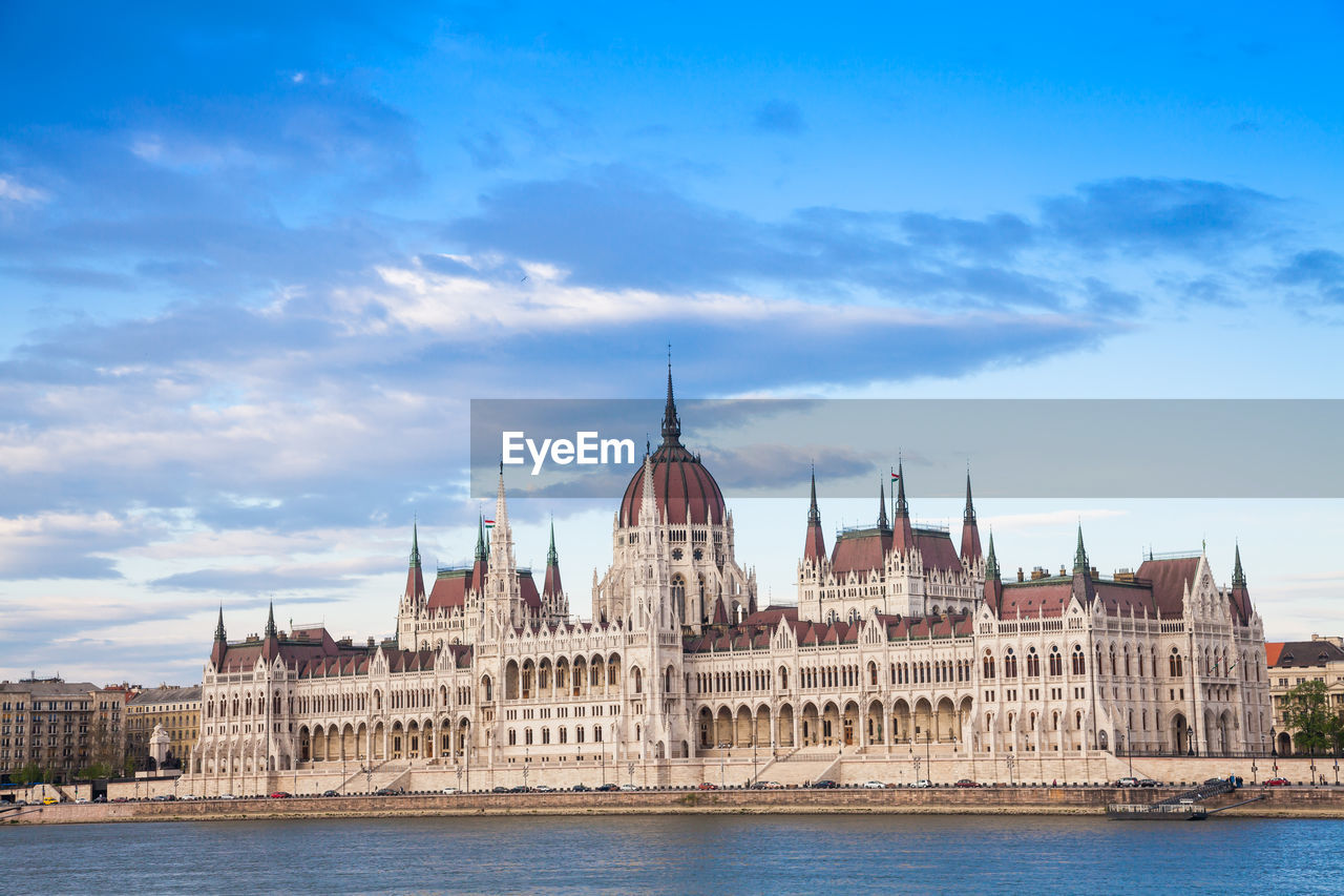 Hungarian parliament building by danube river against sky in city