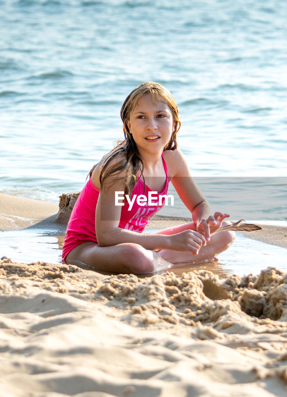 Young girl holds a bird feather, as she decorates a sand castle on the beach