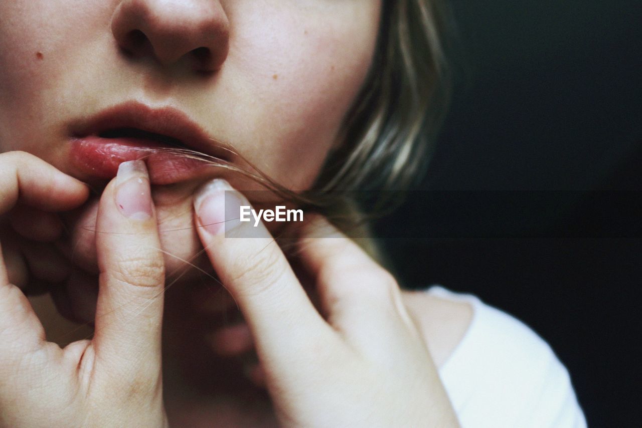 Close-up of woman touching lips against black background