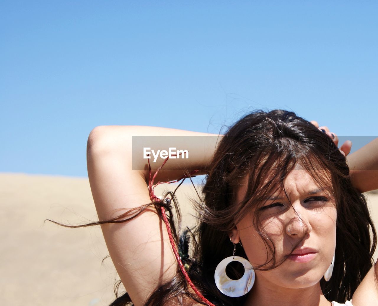 Thoughtful young woman with hands behind head at beach against clear sky