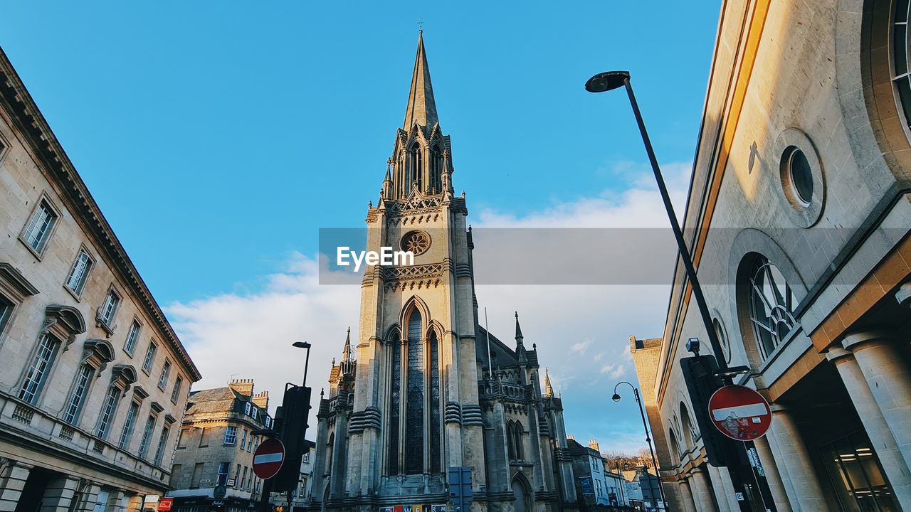 architecture, building exterior, built structure, city, building, travel destinations, sky, tower, landmark, cityscape, urban area, place of worship, religion, travel, history, the past, street, metropolis, tourism, low angle view, nature, belief, downtown, clock tower, spirituality, blue, town, spire, clock, worship, day, time, city street, transportation, catholicism, outdoors, facade, road, no people, city life, clear sky, skyscraper, gothic style, sunny, mode of transportation, cloud