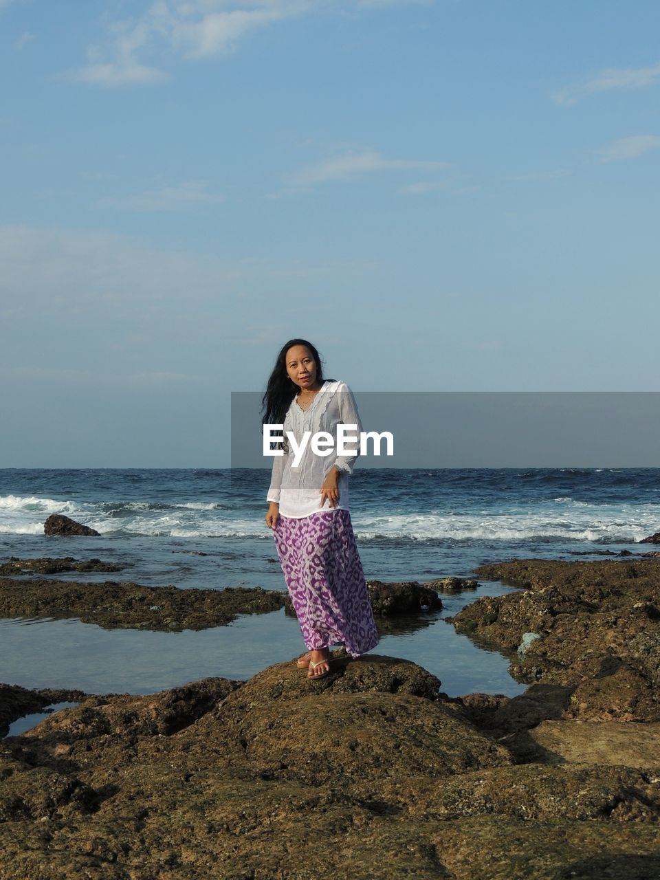 Full length of woman standing on rock at beach against sky
