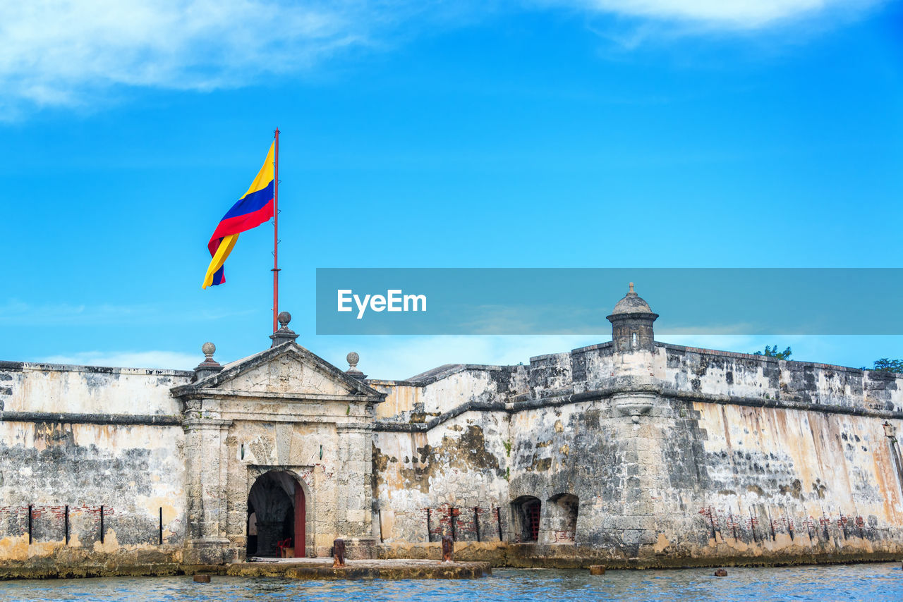 Colombian flag on historic fort by sea against sky