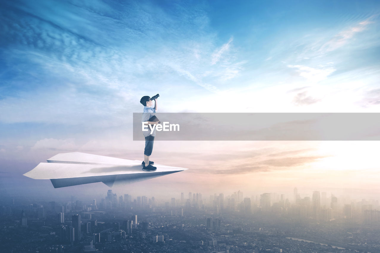 Digital composite image of boy flying on paper airplane over city