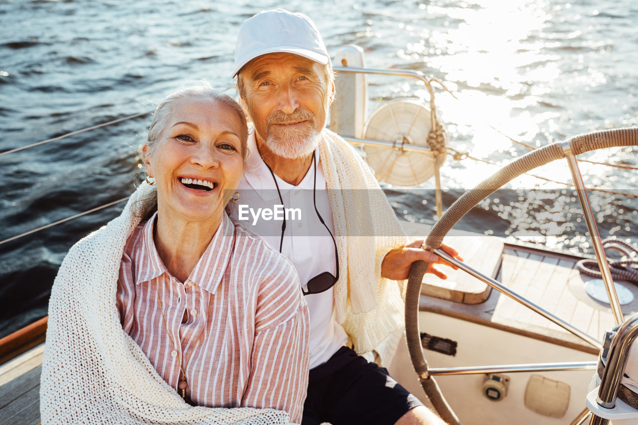 Portrait of smiling couple sitting on sailboat in sea