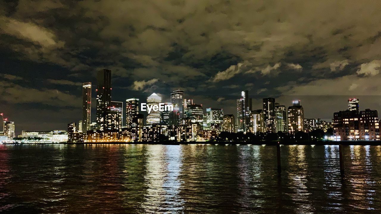 ILLUMINATED BUILDINGS BY RIVER AGAINST SKY