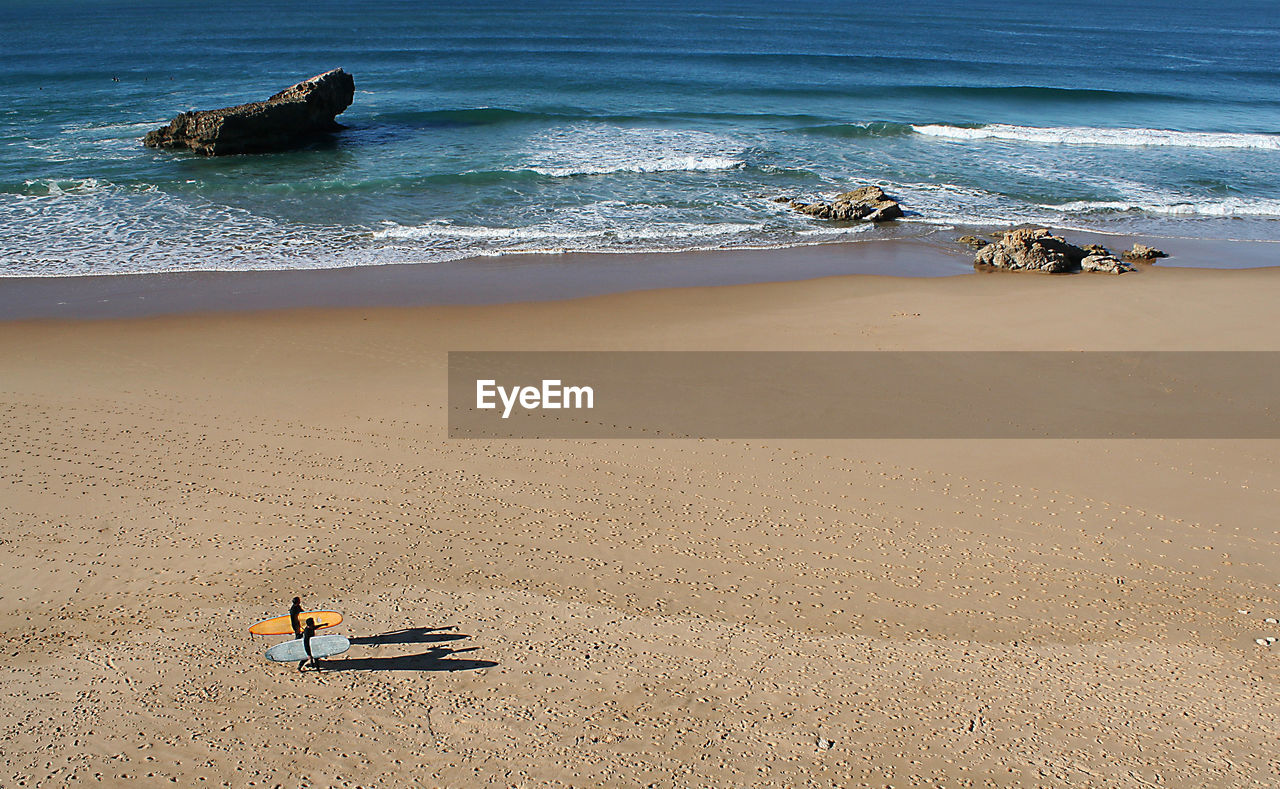 High angle view of people with surfboard walking on sand at beach