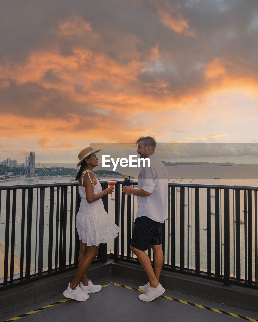 rear view of woman with arms outstretched standing on pier against sky during sunset