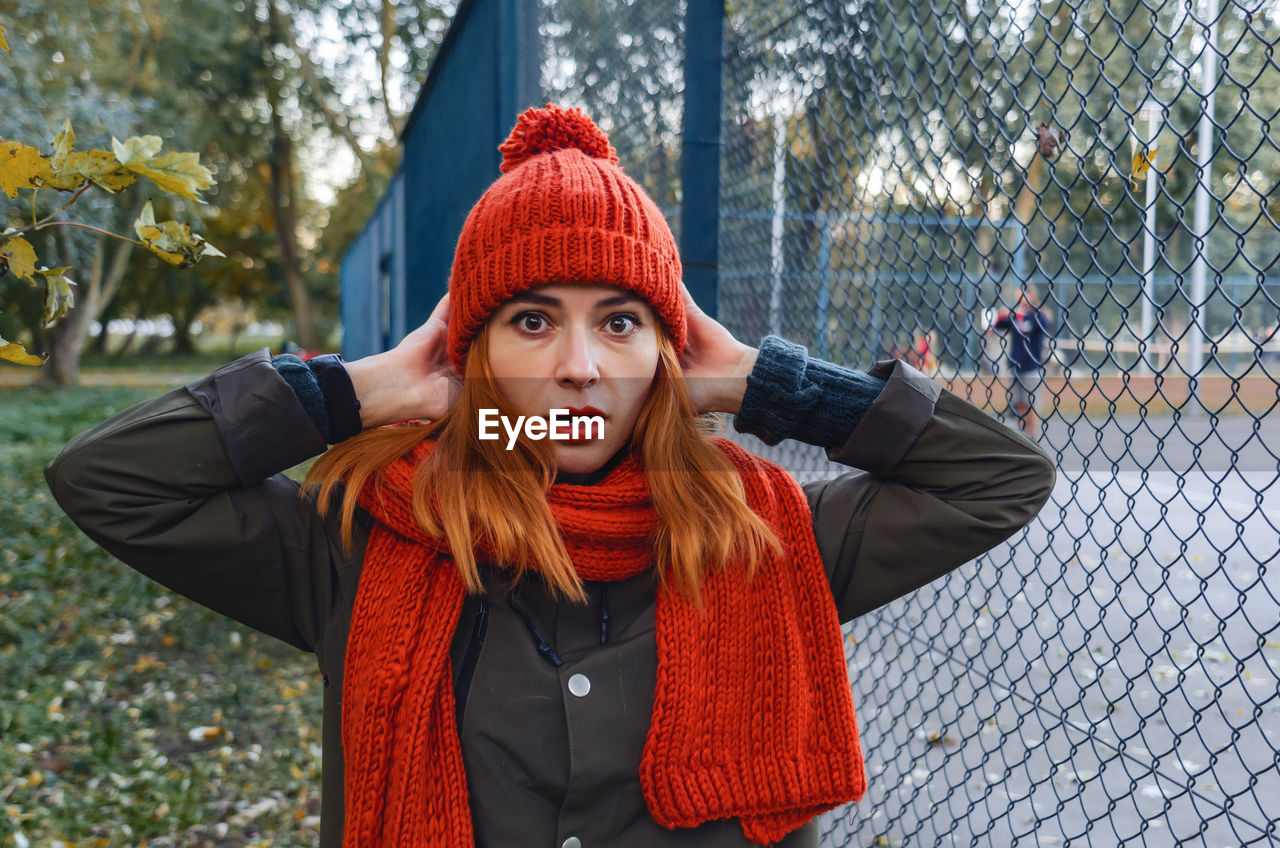 Bright cute young woman in orange warm knitted hat and scarf hands near head. emotion of concern.