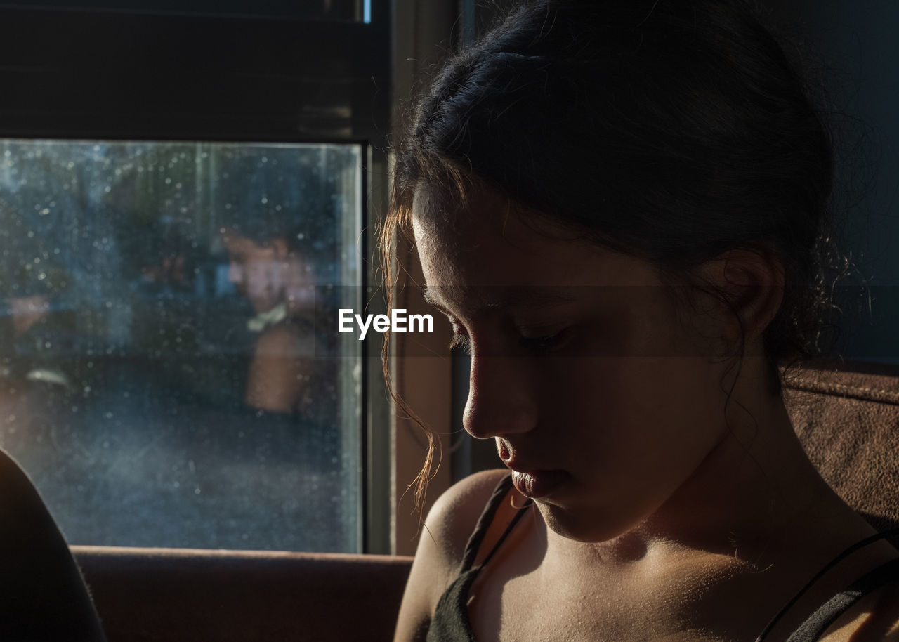 Close-up of young woman looking down near the window