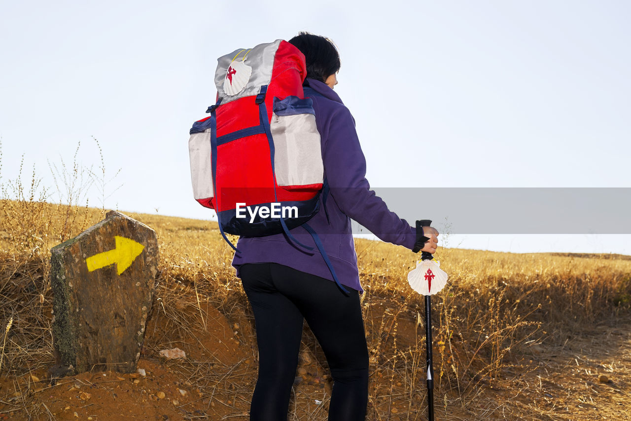 Rear view of female hiker walking on field against clear sky