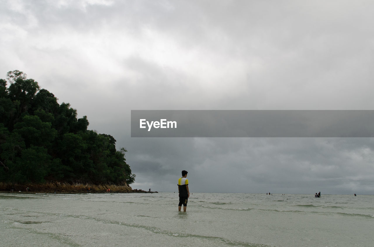 cloud, sky, sea, coast, land, shore, beach, water, ocean, body of water, nature, one person, full length, beauty in nature, overcast, scenics - nature, environment, adult, wave, holiday, vacation, trip, storm, bay, sand, men, outdoors, rear view, leisure activity, day, landscape, horizon, lifestyles, storm cloud, travel, walking, tranquility, travel destinations, wind wave, non-urban scene, wet, plant, solitude, tourism