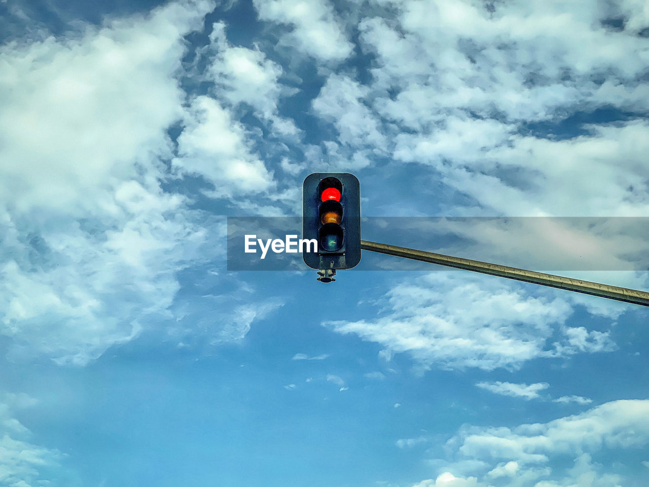 Low angle view of road signal against blue sky with swirling white clouds and copy space.