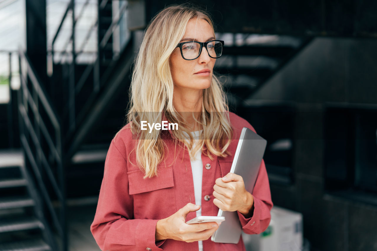 Attractive business woman stands against a modern urban backdrop.