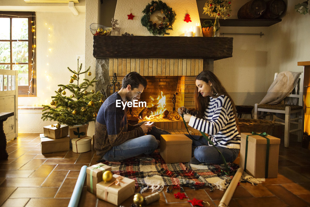 Couple wrapping gift boxes on floor by fireplace at home