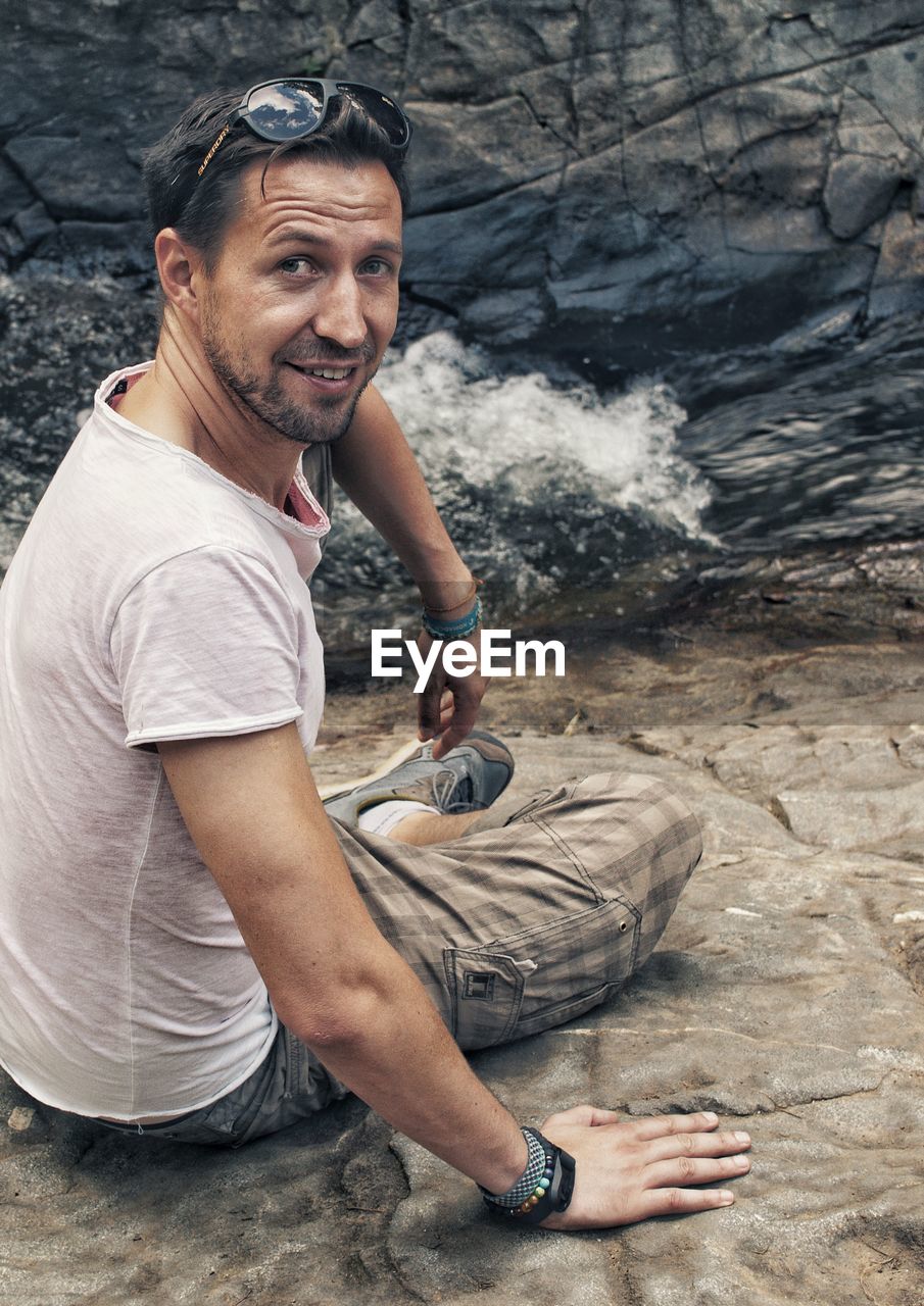 PORTRAIT OF MAN SITTING ON ROCKS