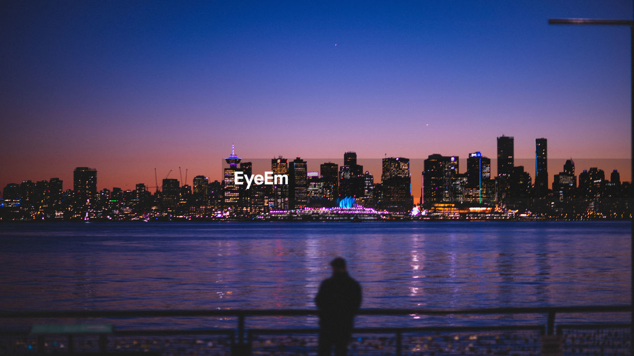 Illuminated city by river against sky at night