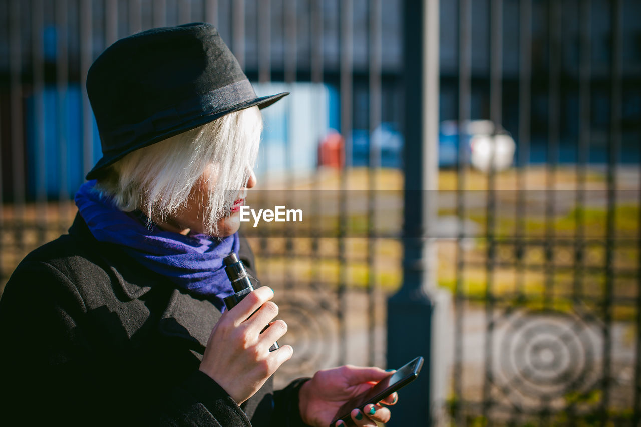 Young woman using mobile phone while smoking at park