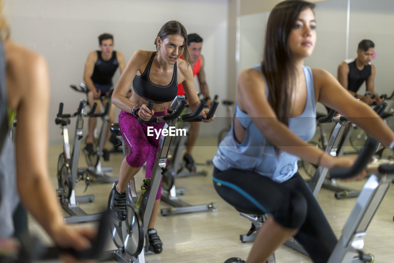 Focused sweaty sportswoman in activewear cycling during group training in spacious fitness center with modern equipment