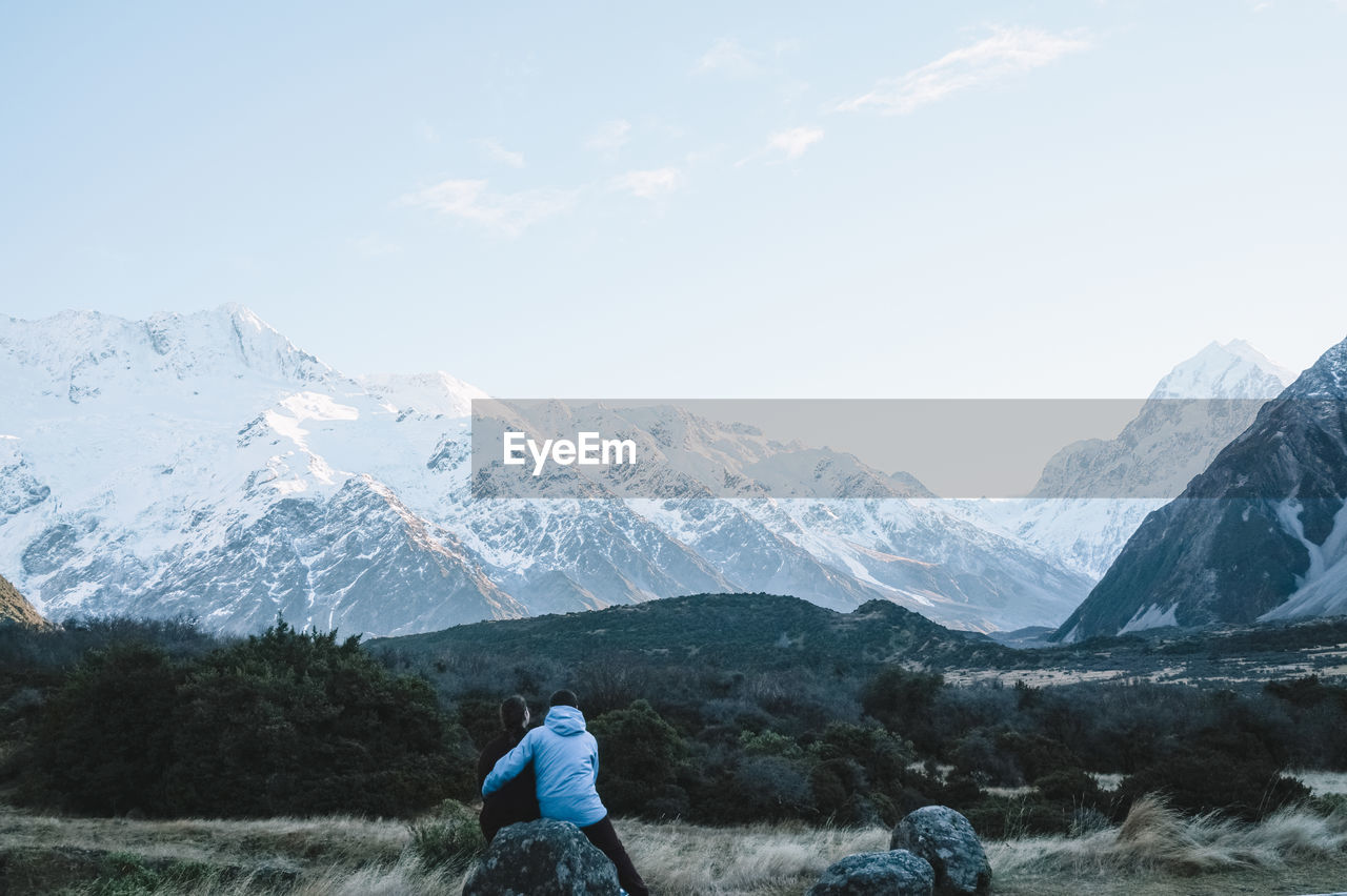 Rear view of couple looking at snowcapped mountains against sky