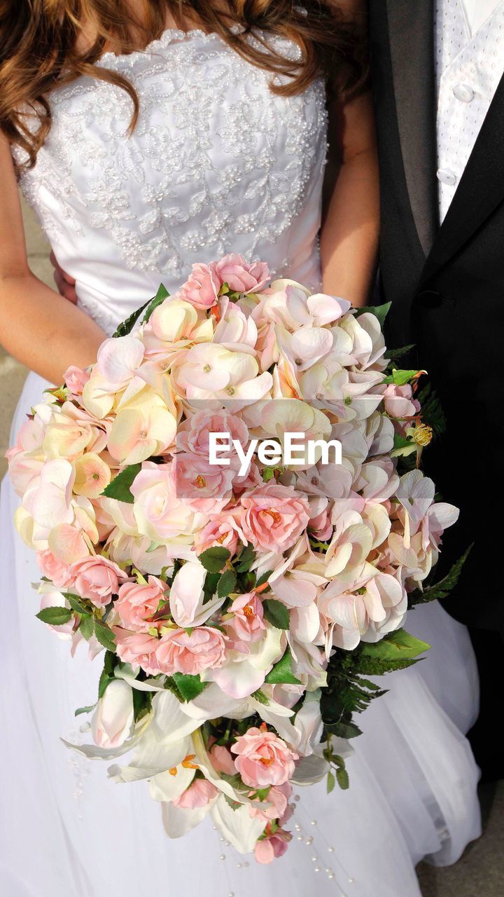 Midsection of bride holding bouquet with groom