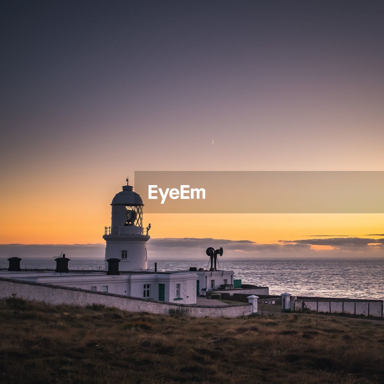 Lighthouse by sea against sky during sunset