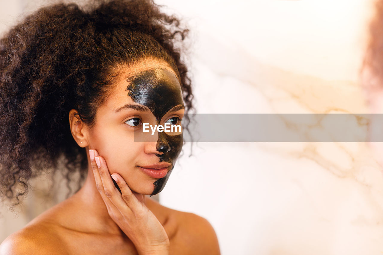 Young woman looking away with facial mask on face against wall