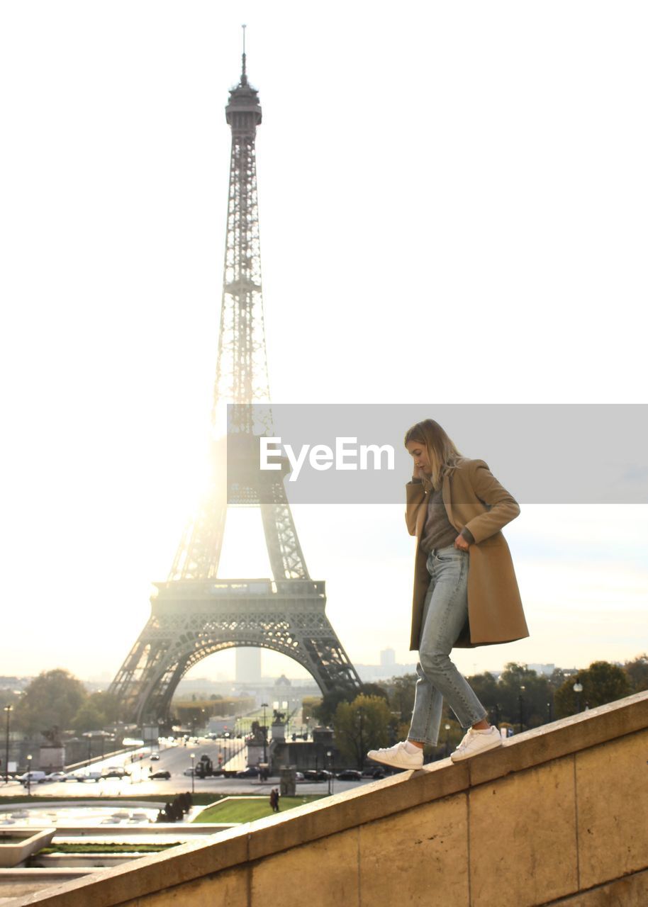 Side view of young woman walking on railing against eiffel tower