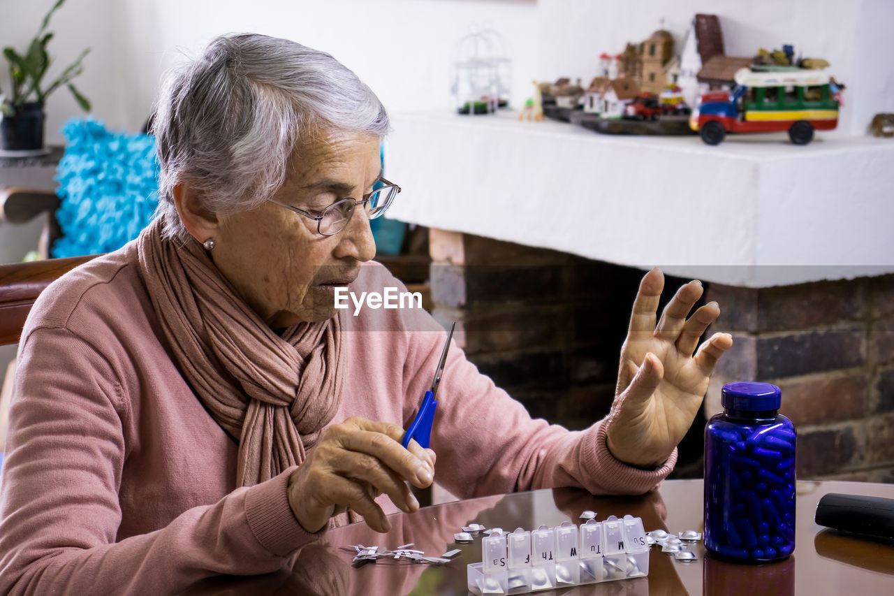 Senior woman taking medicine while sitting by table at home