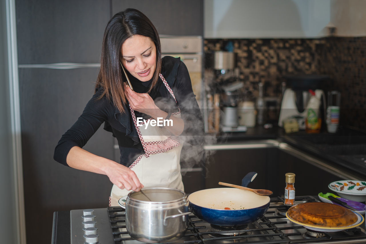 Woman using smartphone while cooking spaghetti in kitchen