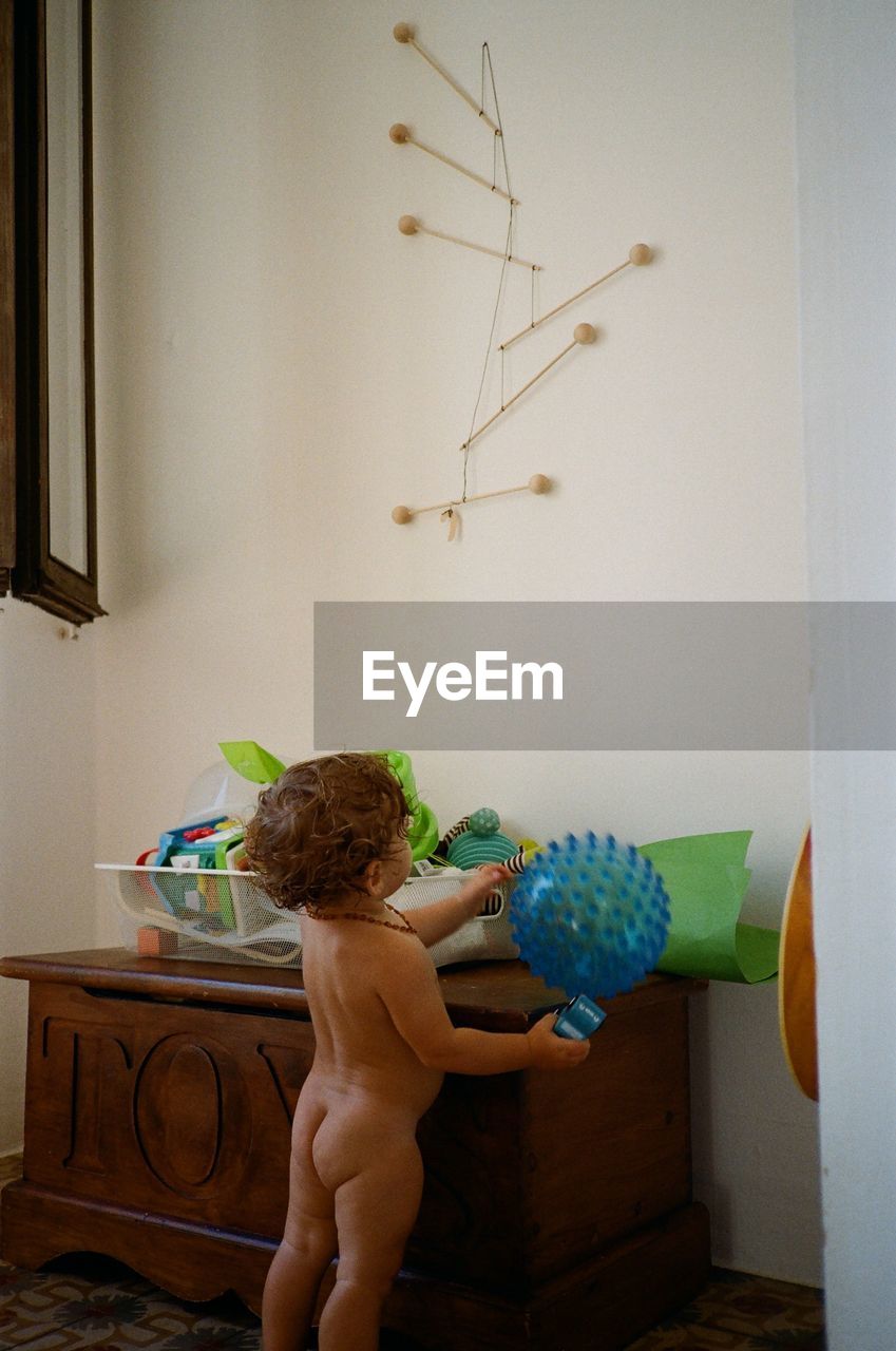 REAR VIEW OF SHIRTLESS BOY AGAINST WALL AT HOME