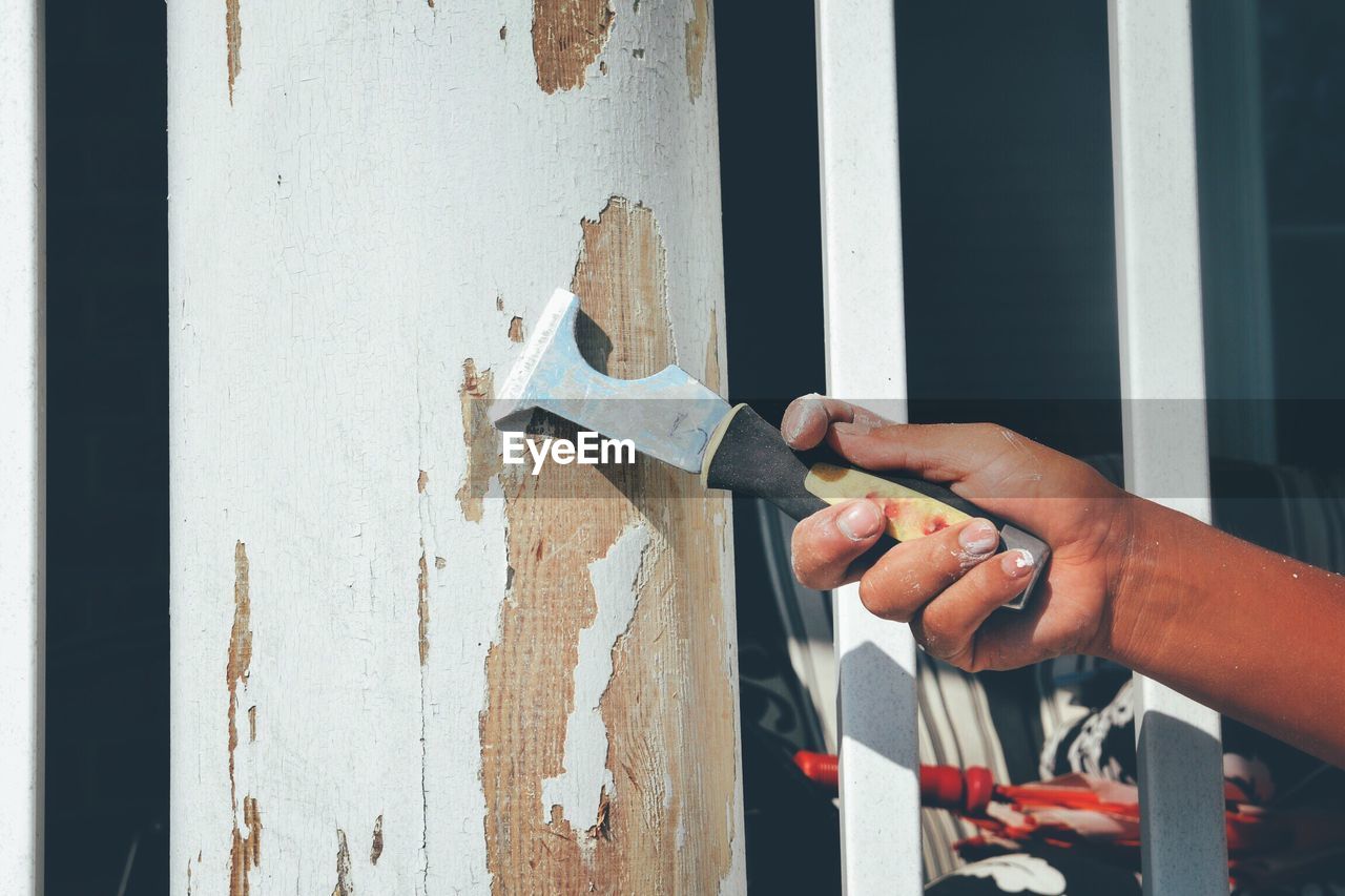 Cropped hand of man scraping paint on wall at home