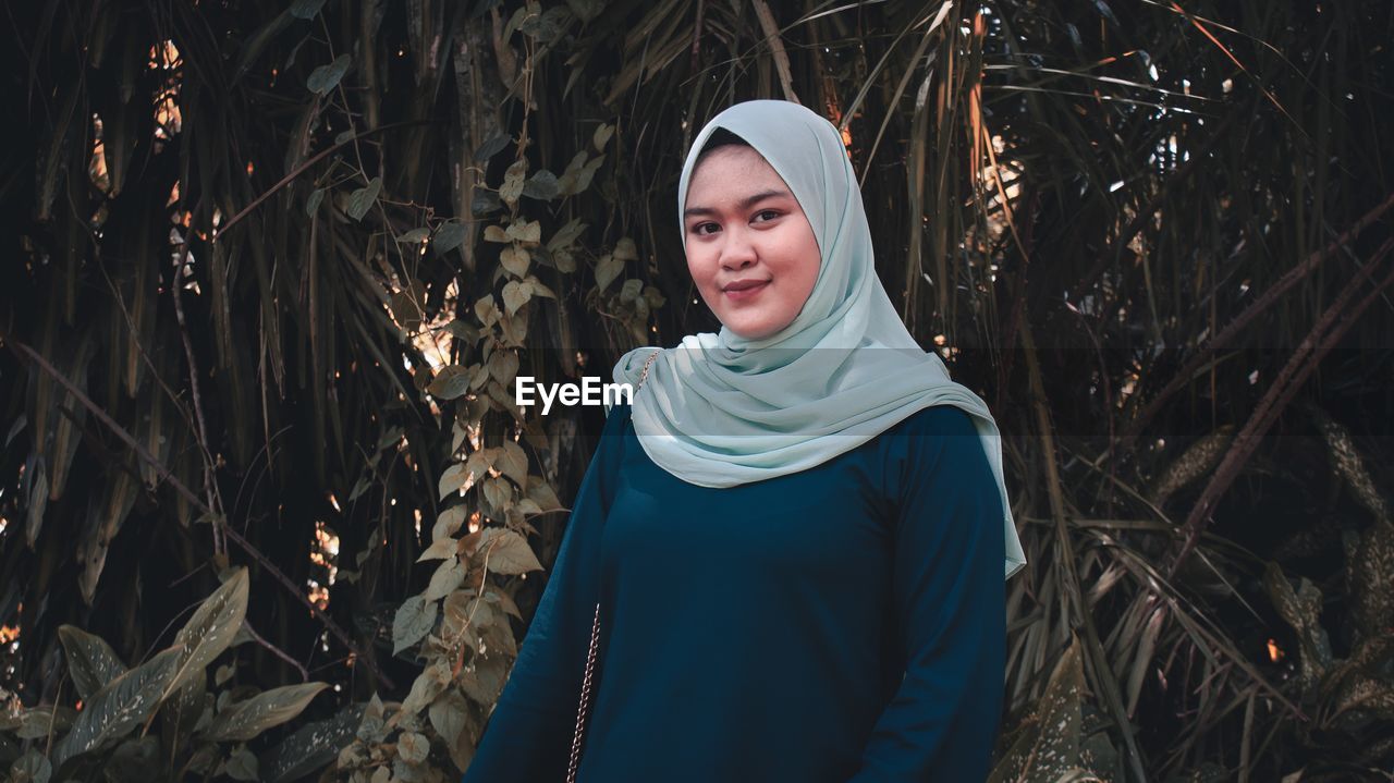 Portrait of smiling young woman standing against trees