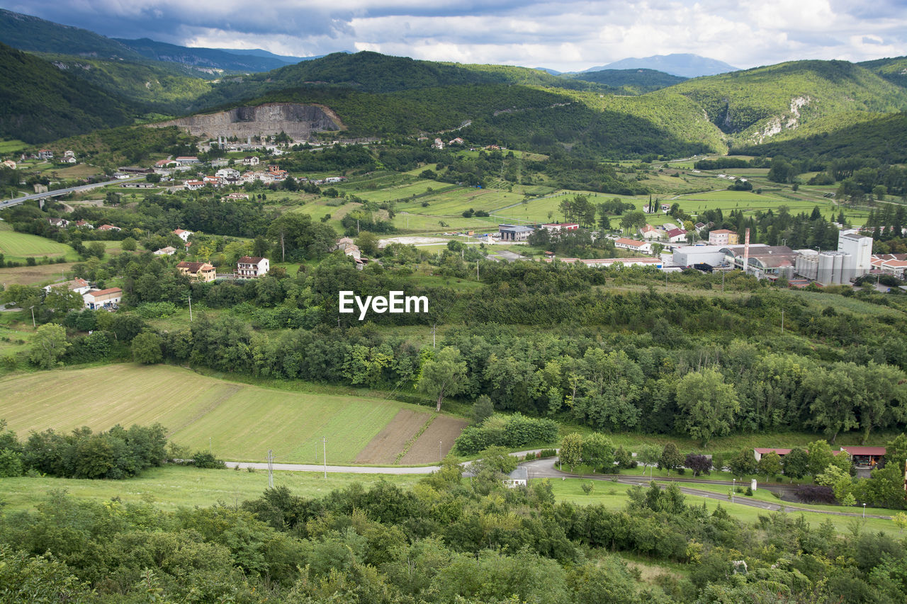 TREES AND HOUSES ON FIELD BY MOUNTAIN