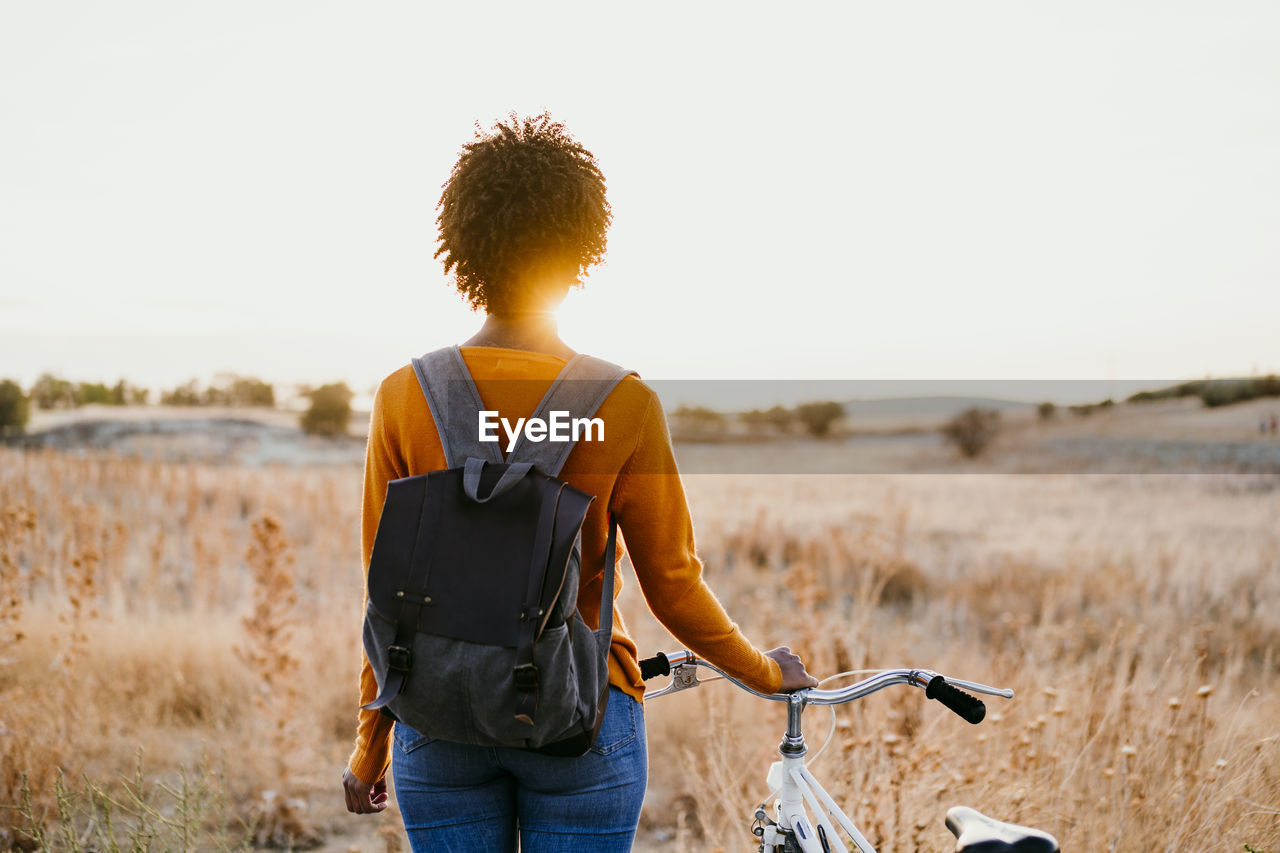 Young woman with bicycle standing in field at sunset