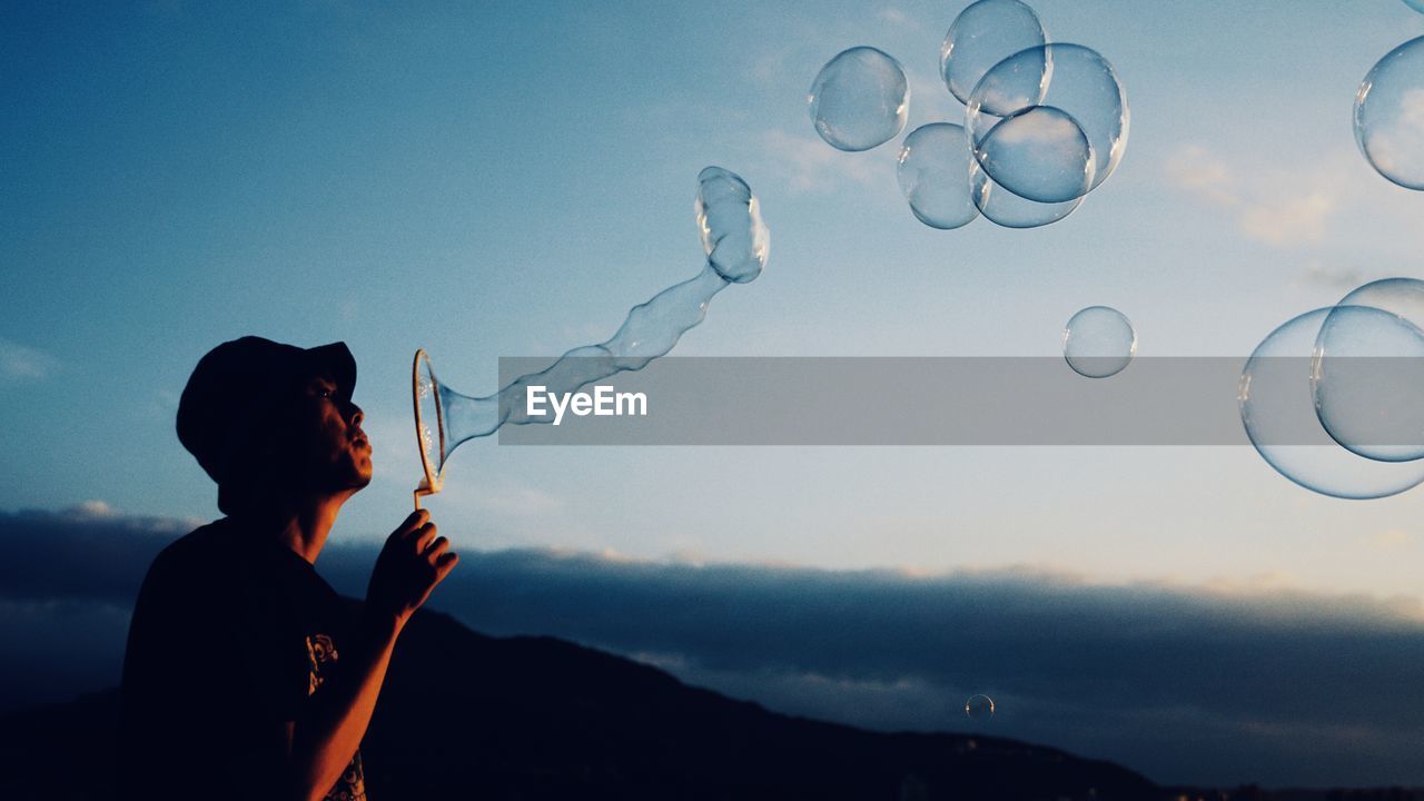 Man blowing bubbles against blue sky