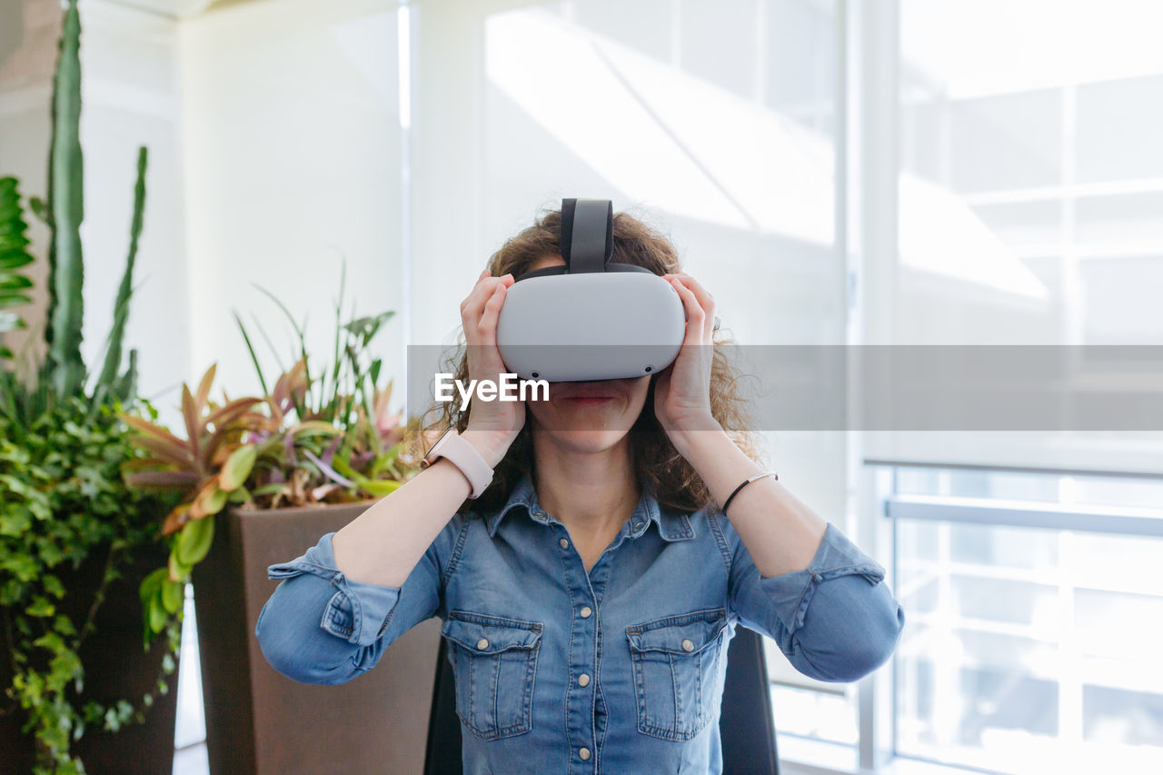 Sitting woman with curly hair trying vr helmet in the office