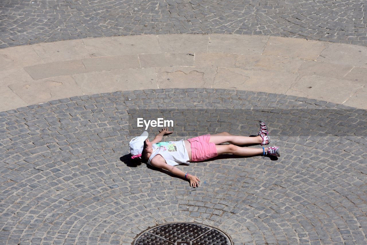 High angle view of girl lying on cobbled street