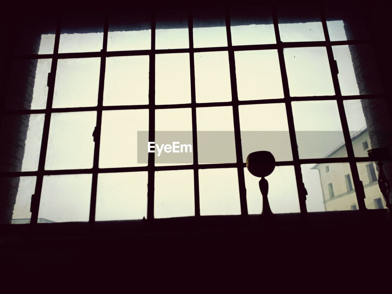 SILHOUETTE MAN STANDING AGAINST SKY SEEN THROUGH METAL GRATE