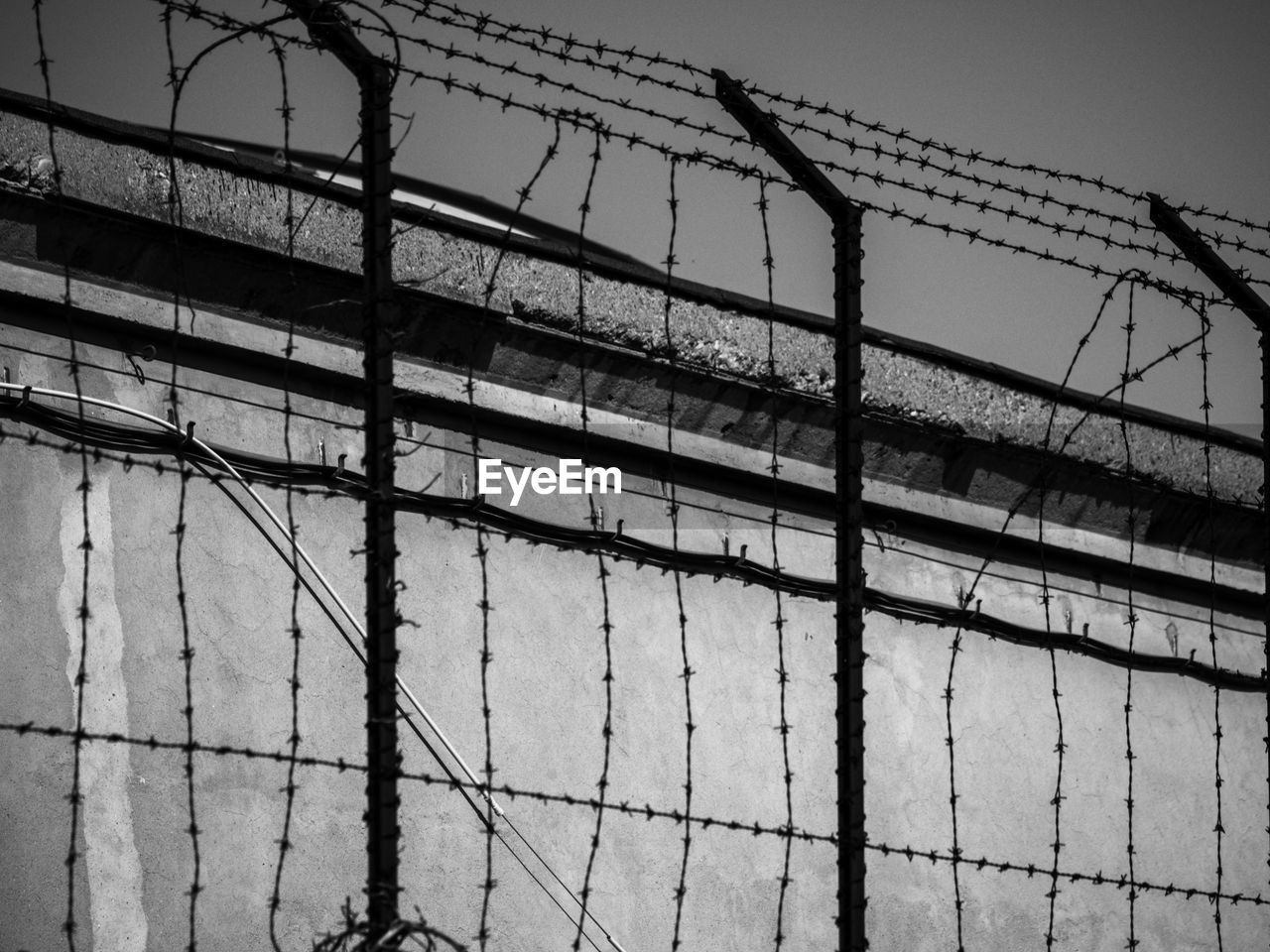 LOW ANGLE VIEW OF BARBED WIRE FENCE AGAINST WALL