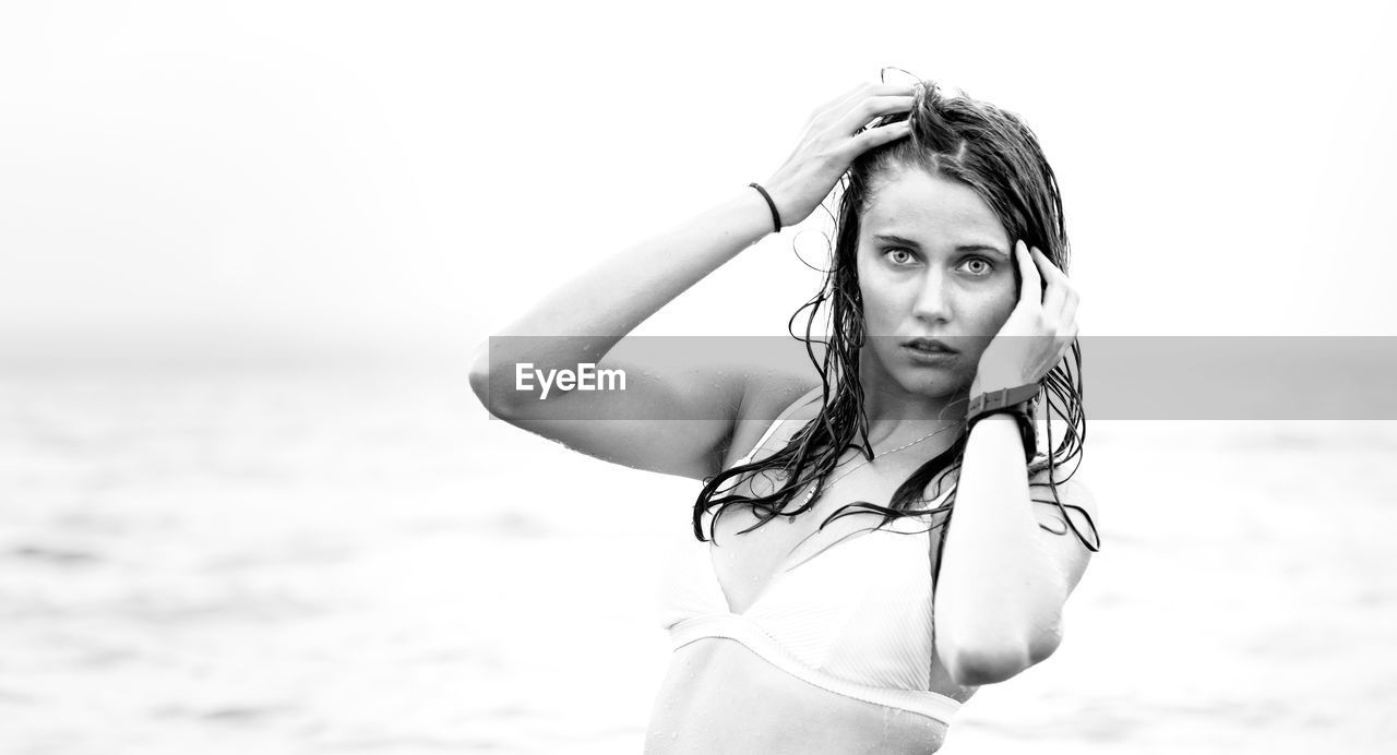 Portrait of young woman standing at beach against sky