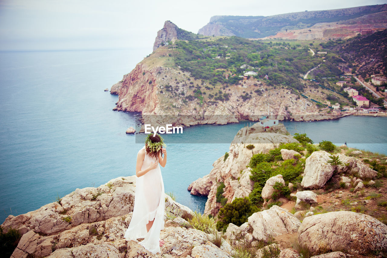 Portrait of a young woman with long hair in a white dress and a wreath on the rock, the mountain