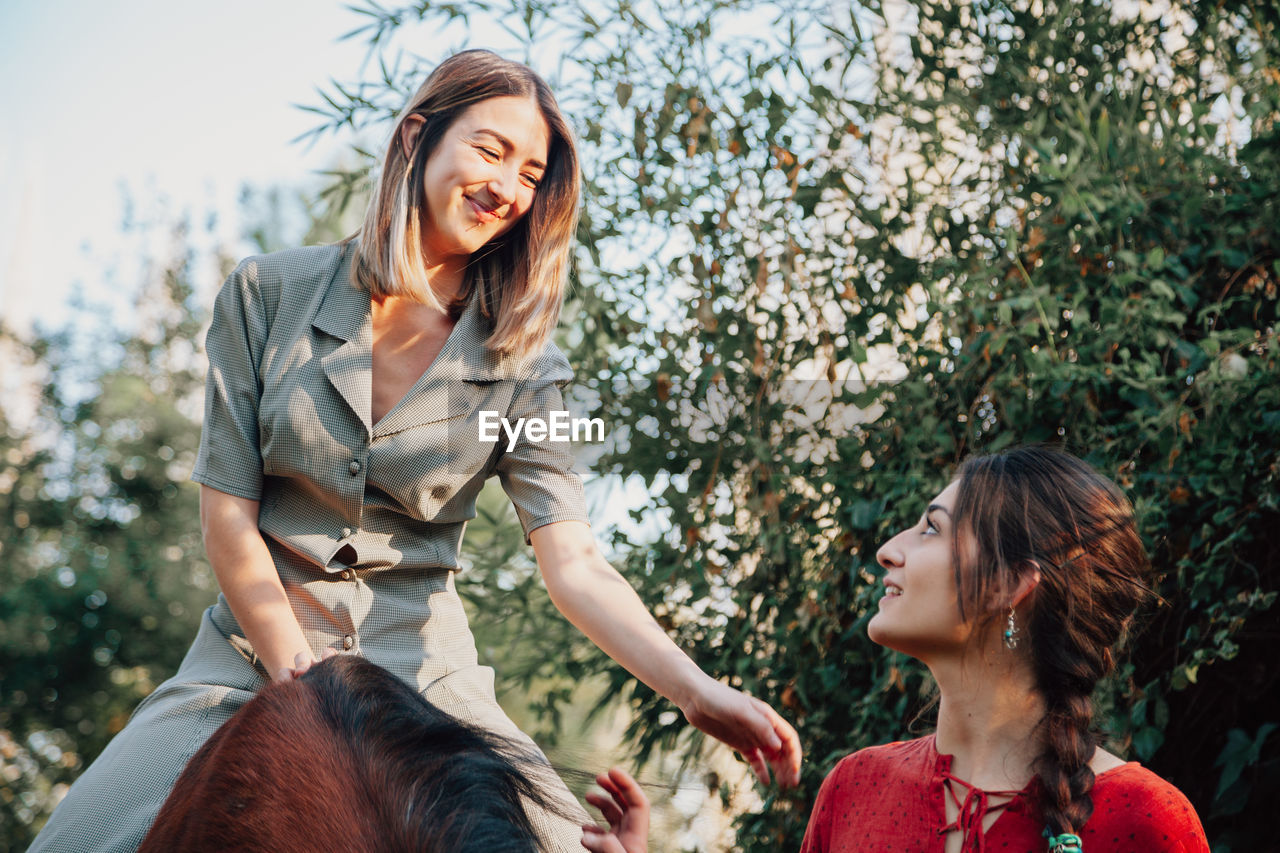 Smiling woman sitting on horse against tree