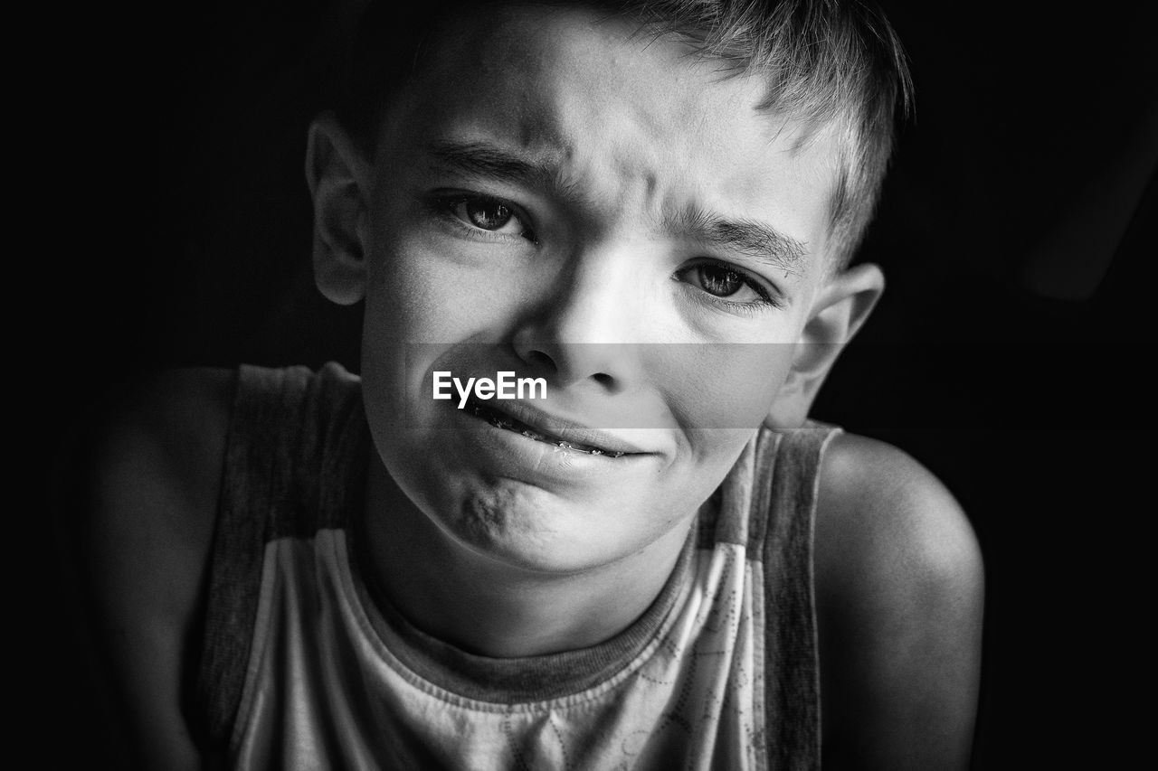 Close-up portrait of boy making face against black background