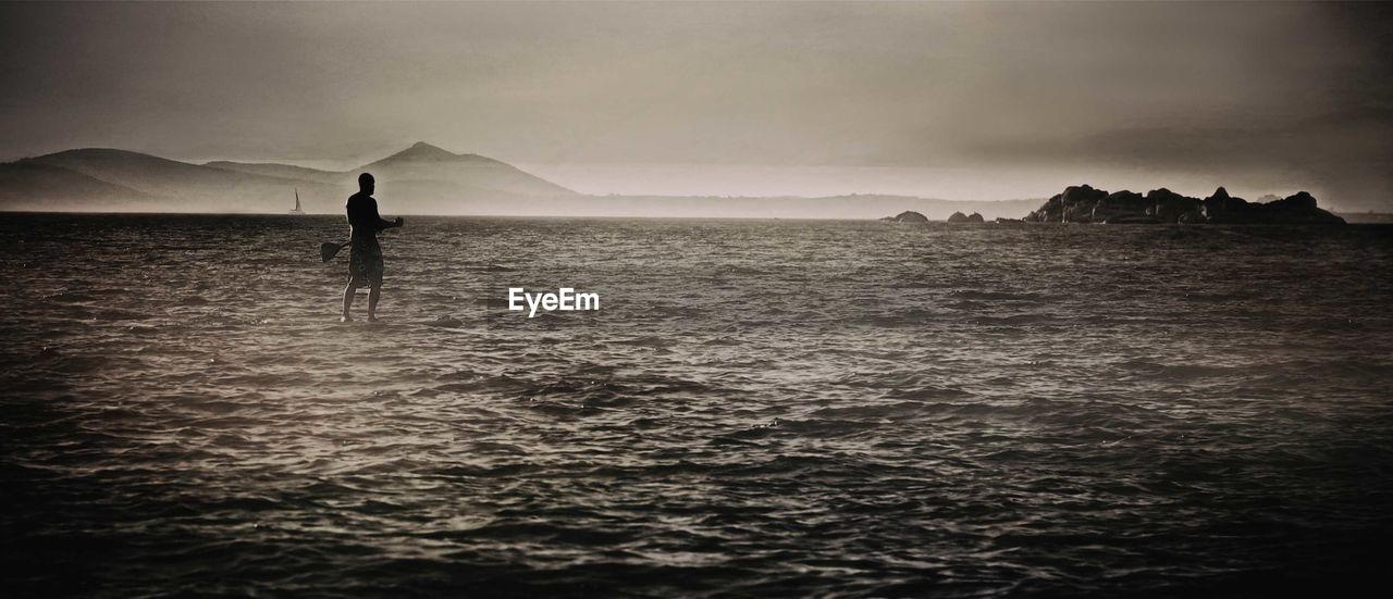 Man paddleboarding in sea against sky